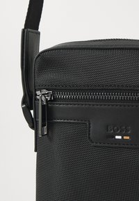 Sac bandoulière noir en nylon texturé et cuir lisse. Fermeture zippée avec quincaillerie en métal argenté et détail de logo embossé.
