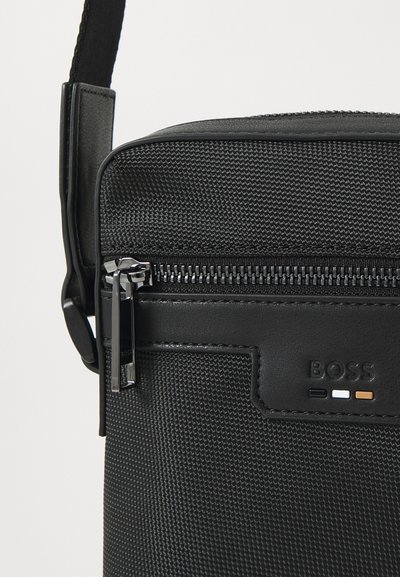 Sac bandoulière noir en nylon texturé et cuir lisse. Fermeture zippée avec quincaillerie en métal argenté et détail de logo embossé.