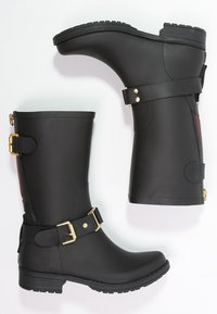 Black rubber boots with a mid-calf height, gold hardware accents, buckle straps, and a textured sole for grip. Features a rear zipper.