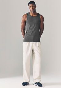 Débardeur gris foncé sans manches, pantalon ivoire à coupe décontractée, et chaussures de sport noires avec des accents blancs. Design simple, texture douce.