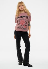 Oversized, faded pink t-shirt with black graphic print and text, paired with black flared jeans and black ankle boots, featuring frayed hem.