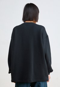 Svart oversized sweatshirt med rund halsringning, sänkta axlar och långa ärmar. Mjuk textur, minimalistisk design, avslappnad passform.