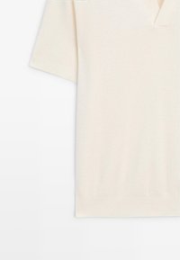 Crème top met korte mouwen en V-hals, gemaakt van een structuurgebreide stof, met subtiele ribbelaccenten bij de kraag en zoom.