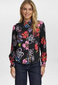 Camicetta nera floreale con fiori vivaci in rosa, rosso e blu, dotata di colletto a bottoni e maniche lunghe arricciate.