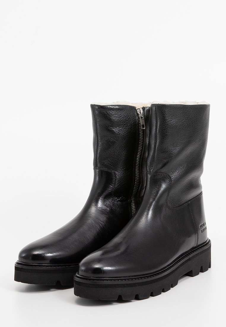 Een paar zwarte leren laarzen tot halverwege de kuit met een zijrits, een stevige robuuste zool en witte fleece voering.