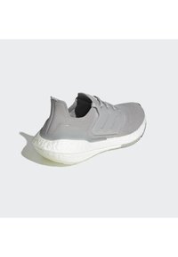 Scarpa sportiva grigia con tomaia in maglia testurizzata, dettaglio a tre strisce e suola bianca ammortizzata. Presenta un design a basso profilo e una calzata flessibile.