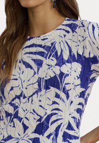 Knit sweater featuring a white base with a blue floral pattern, ribbed texture, round neckline, and short sleeves.