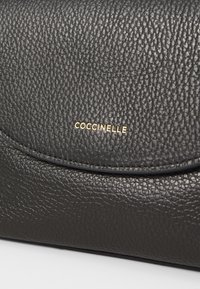 Borsa a tracolla in pelle nera textured con chiusura a patta e dettagli del logo in oro. Presenta una finitura liscia e un leggero motivo a grana.
