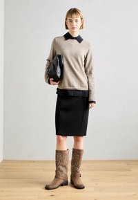 Suéter beige de mezcla de lana, camisa negra con cuello debajo, falda lápiz negra, botas marrones hasta la rodilla con tachuelas decorativas, bolso de mano negro.