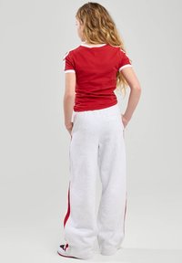 Camiseta roja de manga corta con ribete blanco y pantalones de chándal grises de pierna ancha con franjas laterales rojas, vistos desde atrás.