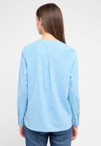 Himmelbluse mit kleinen weißen Punkten, langen Ärmeln, einem runden Ausschnitt und einem dekorativen Knopfdetail auf der Rückseite.