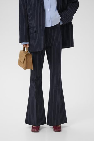 Navy pinstriped suit with flared pants, paired with a light blue shirt. Accessories include a tan handbag and maroon heeled shoes.