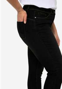 Jeans de mezclilla negra con un ajuste slim, que cuentan con una cintura de altura media, bolsillos tradicionales y detalles de costura en contraste a lo largo de las costuras.