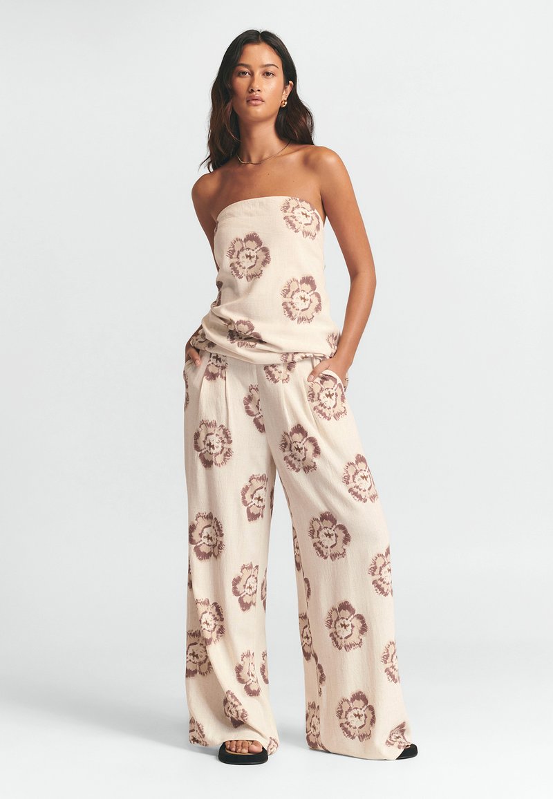 Beige strapless topp med blommönster, matchat med löst sittande krämfärgade byxor som har liknande blommönster. Mjukt, strukturerat tyg.