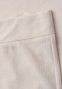 Gros plan sur un tissu tricoté beige clair avec un motif gaufré texturé et un détail visible de couture.