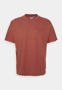 T-shirt à manches courtes, col rond, de couleur rouille, en coton, avec un logo subtil dans la partie supérieure gauche. Texture douce.