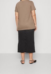 Brun kortärmad skjorta och svart denim midi-kjol med rak skärning och subtil textur. Svarta platta sandaler kompletterar outfiten.