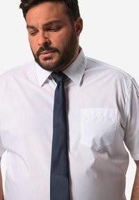 Camisa de vestir blanca de manga corta con collar abotonado, que presenta un bolsillo en el pecho izquierdo, combinada con una corbata de color azul marino oscuro. Textura de tela suave.