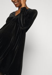 Černé sametové těhotenské šaty s výstřihem do V, dlouhými puff rukávy, nařaseným živůtkem a volnou sukní. Měkká textura, délka po kolena.