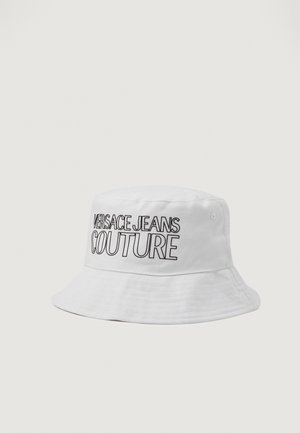 Hvit bøttehatt laget av teksturert stoff med en fremtredende svart "VERSACE JEANS COUTURE"-logo foran.