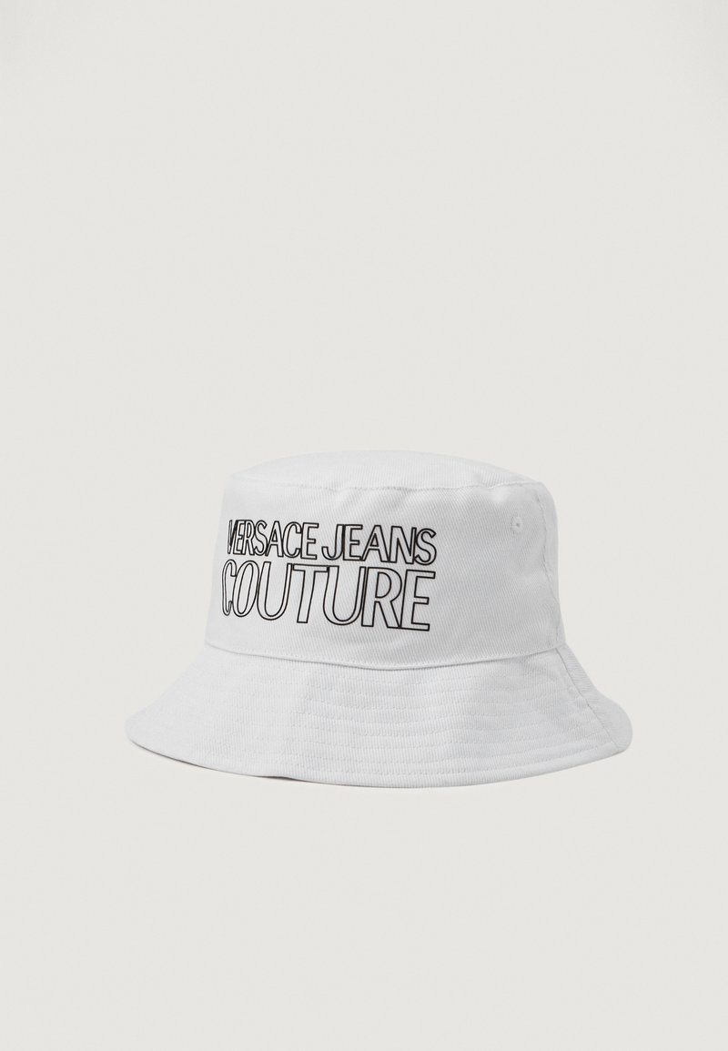 Biela čiapka s okrajom vyrobená z textúrovaného materiálu, na prednej strane má výrazné čierne logo "VERSACE JEANS COUTURE".