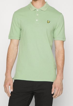 Light green polo shirt made of cotton, featuring a collar, three buttons, and a small yellow logo on the left chest. Short sleeves.