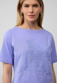 Lichtpaarse shirt met korte mouwen en een paillettenbladpatroon op de voorkant. Zacht materiaal met een ronde halslijn en een relaxte pasvorm.