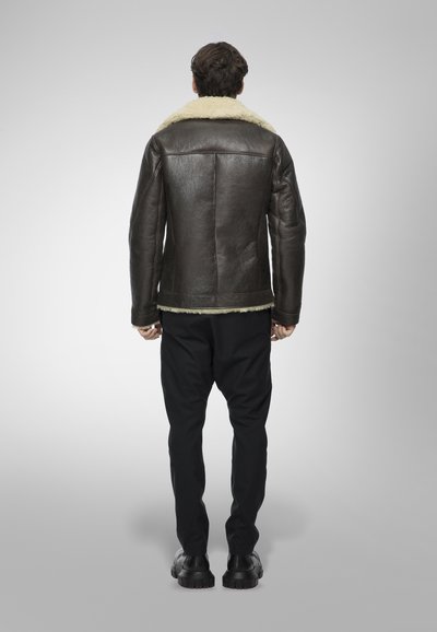 Giacca di pelle marrone con colletto in shearling, finitura strutturata, design aderente e pantaloni neri. Dettagli hardware lisci visibili.