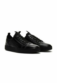 Sneaker nere in pelle con lati testurizzati, chiusura con lacci, linguette e suola piatta in gomma. Punta liscia e accenti a contrasto.