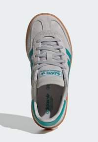 Grijze suède sneaker met teal accenten, ronde neus en witte veters. Bruine rubberen zool en merklogo op de tong. Vlak ontwerp en textuur oppervlak.