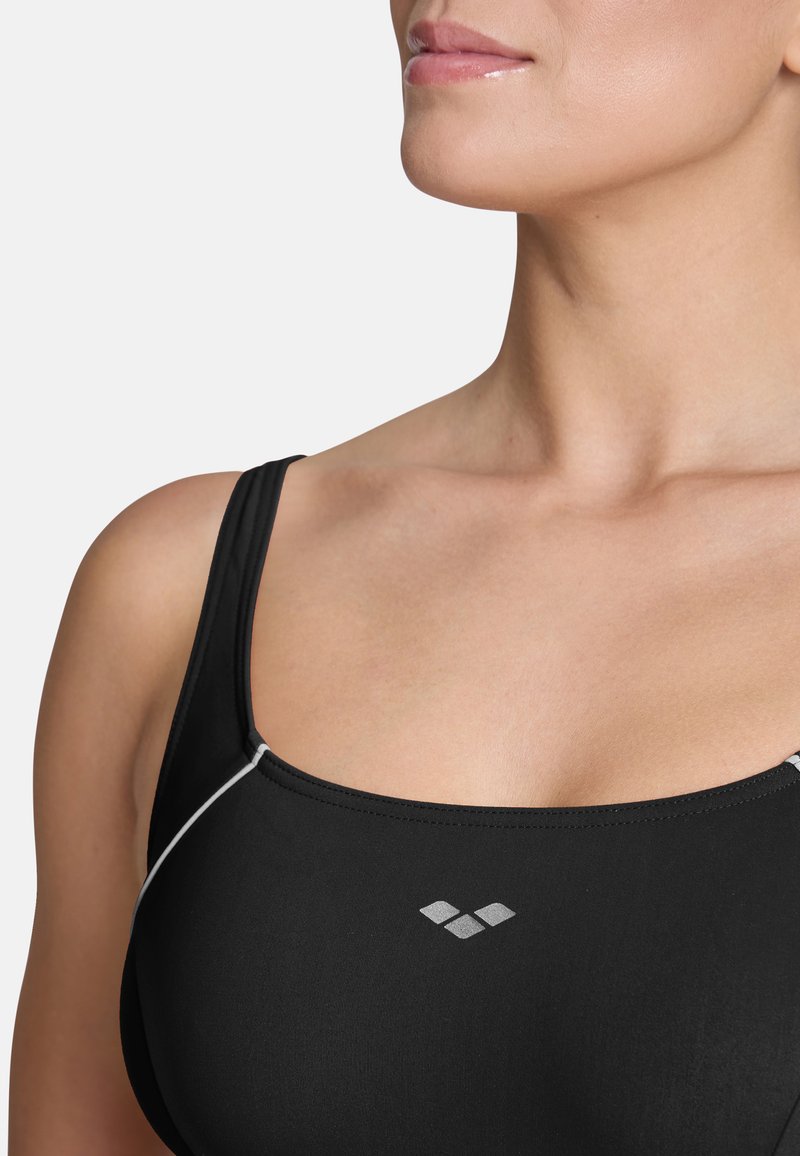 Soutien-gorge de sport noir avec des fines bretelles, présentant un décolleté arrondi et des coutures d'accent blanches. Embelli d'un petit logo en argent à l'avant.