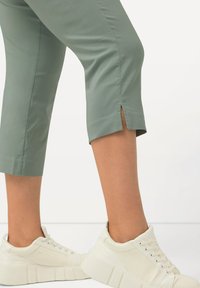 Pantalons cropped vert clair avec fentes sur les côtés, associés à des baskets blanches texturées avec une semelle épaisse et striée.