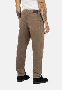 Brown corduroy pants with two back pockets and a leather waistband patch. Worn with black shoes, featuring a straight leg design.