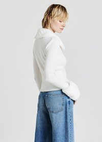 Top bianco a coste con collare e polsini in peluche bianchi, abbinato a jeans a gamba larga blu chiaro, mostrato di schiena su uno sfondo neutro.