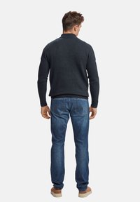 Temno siva pletena jopica z visokim ovratnikom, v kombinaciji z modrimi denim hlačami. Outfit dopolnjujejo svetlo rjave superge.