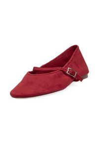 Zapato plano de ante rojo con punta afilada, una correa en el tobillo con una hebilla metálica y una suela baja marrón. Textura suave y diseño minimalista.