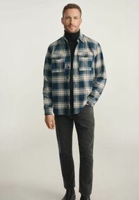 Koszulka w kratę w kolorze niebieskim i białym, ozdobiona dwoma kieszeniami na piersi i zapięciem na guziki, noszona na czarnym golfie, w połączeniu z ciemnymi dżinsami.