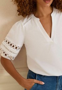 Witte blouse met korte, uitgeblazen mouwen en gedetailleerde oogjes uitsparingen. V-hals ontwerp en een soepele textuur, gecombineerd met hoge taille denim broek.