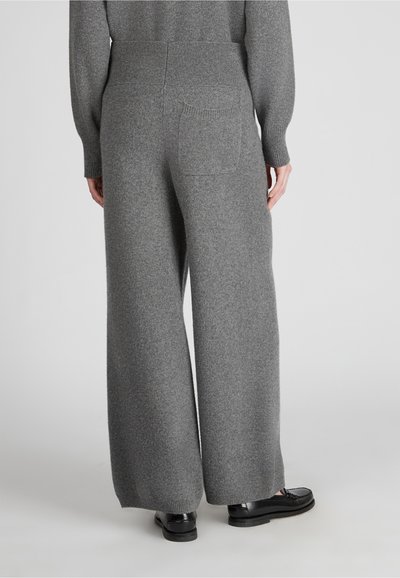 Weite graue Wollhosen mit einem gerippten Bund, ausgestattet mit einer Gesäßtasche und einer weichen, strukturierten Oberfläche. Kombiniert mit schwarzen Slippern.