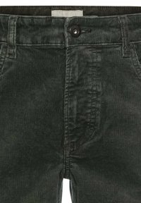 Pantalon en velours côtelé vert avec une surface texturée, doté d'une fermeture à bouton à l'avant et d'une petite étiquette au niveau de la taille.