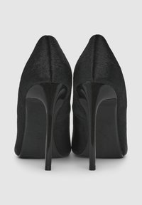 Scarpe nere con tacco alto caratterizzate da una forma affilata e un materiale dalla superficie liscia, con tacchi a stiletto neri lucidi e un dettaglio di branding discreto.