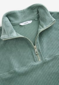 Grønne corduroy quarter-zip pullover med ribbet tekstur, udstyret med en metallynlås og krave, mærket "NEXT" indeni.
