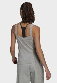 Débardeur de sport sans manches gris clair avec une texture douce, un col rond, et un design dos nageur noir superposé en dessous.