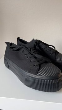 Black canvas sneakers with a thick ribbed rubber sole, round toe cap, and flat laces. Features a smooth upper and contrasting toe detailing.