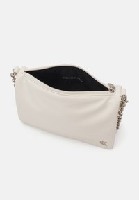 Borsa a tracolla Calvin Klein Jeans, realizzata in morbido materiale color crema. Presenta una chiusura con zip, una tracolla a catena e un accento con logo in rilievo.
