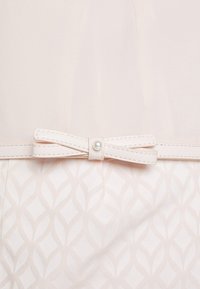 Robe rose clair avec une couche supérieure transparente, un bas à motif, et une ceinture décorative avec un nœud et un accent en perle à la taille.