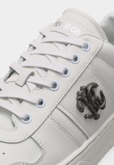 Λευκό δερμάτινο αθλητικό παπούτσι με λευκά κορδόνια, μεταλλικό έμβλημα φιδιού στο πλάι και μερικώς ορατό κεντημένο κείμενο της μάρκας στη γλώσσα.