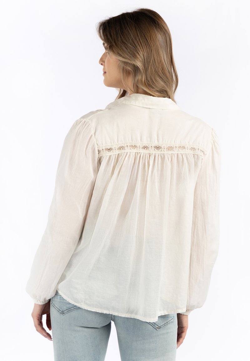 Blusa chiara e morbida con colletto, retro arricciato e delicati dettagli in pizzo lungo lo scollo. Realizzata in un tessuto trasparente.