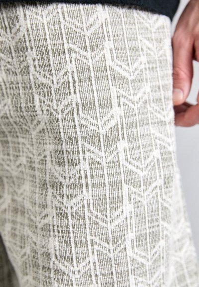 Texturiertem Gewebe mit einem geometrischen Pfeilmuster in gedämpften Beige- und Weißtönen, hergestellt aus einem weichen, gewebten Material.