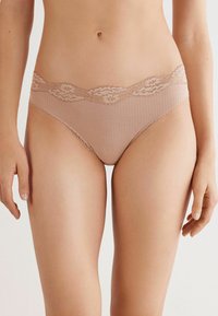 Lace, beige hipster ondergoed met een gegolfde tailleband, voorzien van een geribbelde textuur en delicate bloemenkant aan de bovenrand.